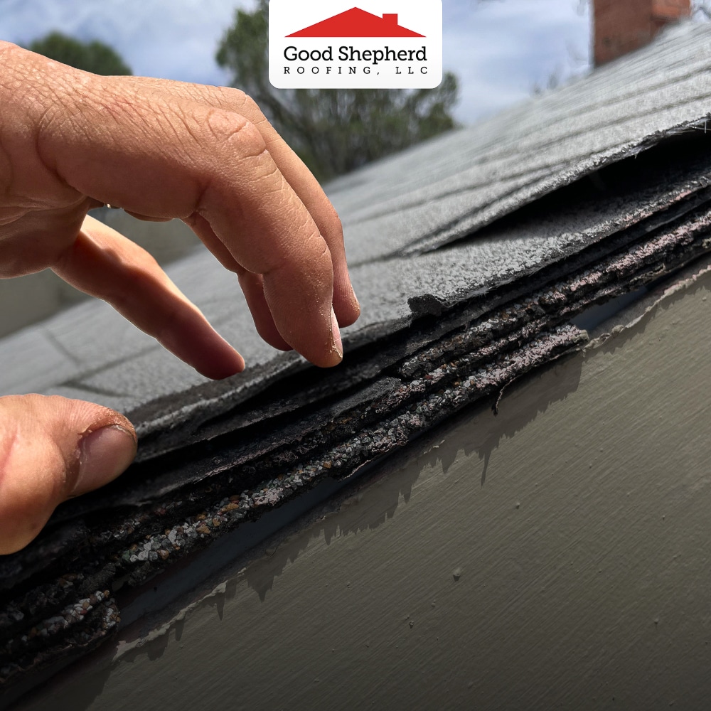 Close-up of hand lifting old roof shingles, showing multiple layers beneath the top roof surface.
